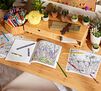 Wildflowers Coloring Book. Open book with partially colored page on table along with additional coloring pages and colored pencils.